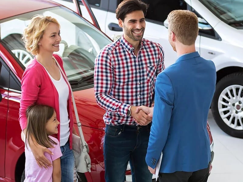 Salesperson having Handshake with Customer Family Standing in Front of Vehicle